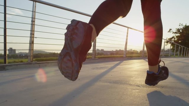 SLOW MOTION: Female runner running across city bridge into magical rising sun