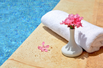 Decorative vase with pink flowers and a white towel at the pool 