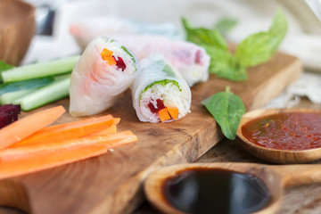 Raw Vietnamese rice spring rolls on wooden board served with soy and chili sauces. Selective focus. Blurred background