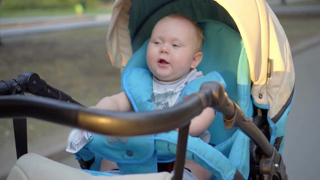 The kid rides in a carriage and waving hands of the packages with baby food in their hands.