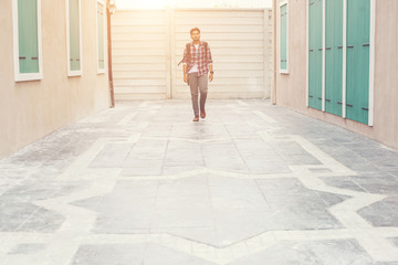 Young hipster man walking on urban street with backpack on his s