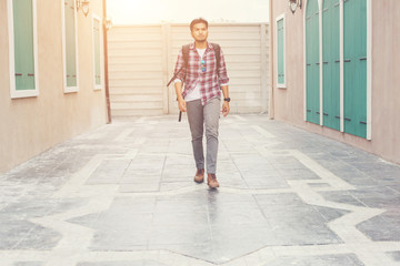 Young hipster man walking on urban street with backpack on his s