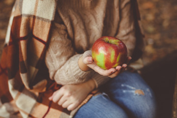 A woman with a plaid on his shoulders holding ripe red Apple