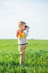 Little boy with an old camera shooting outdoor. Kid taking a photo using a vintage retro film cam. Green summer field.