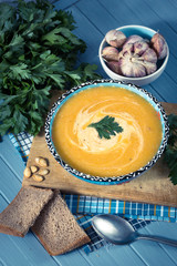 cream soup with pumpkin, greens, seeds and bread on a blue backg