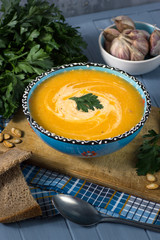 cream soup with pumpkin, greens, seeds and bread on a blue backg