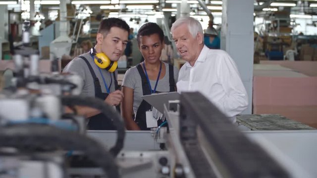 Elderly factory supervisor talking with female Latin-American worker and her Asian colleague about new machinery 