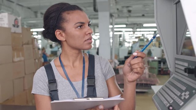 Latin-American factory worker writing down data from control panel 