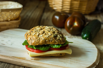 Healthy sandwich with cheese, tomatoes, lettuce on wood cutting board, rustic style, close up