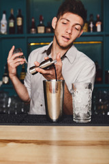 Young handsome barman pouring cocktail drink into glass