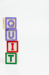 QUIT word wooden block arrange in vertical style on white background and selective focus
