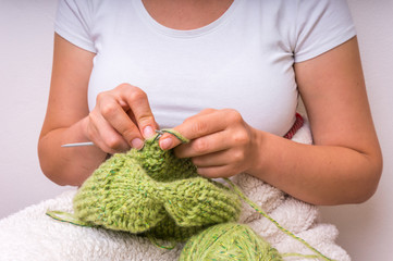 Woman hands with needles knitting with green wool