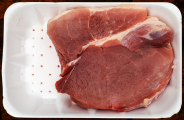 Raw meat, ham, lies in a white plastic tray in one piece.