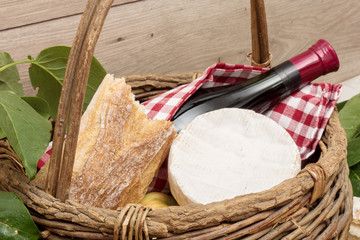 Camembert cheese in a basket with bottle of wine and bread