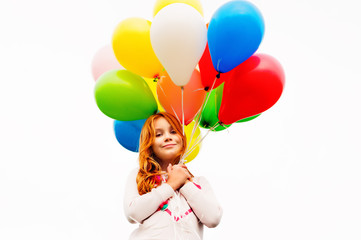 Fototapeta na wymiar Happy little 8-9 year old girl with red hair holding colorful helium balloons