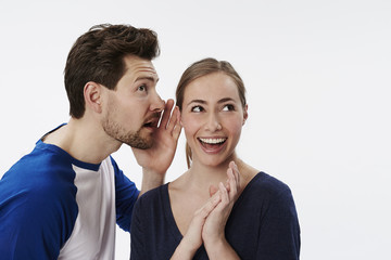 Man whispering to excited woman, studio