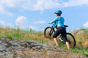 Naklejka premium Female cyclist with her mountain bike climbing up a rock on foot