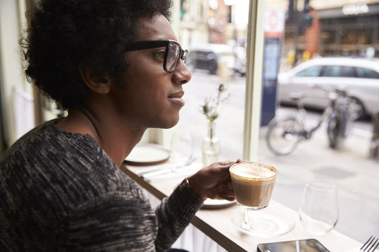 Young man looking through window while having coffee in cafe