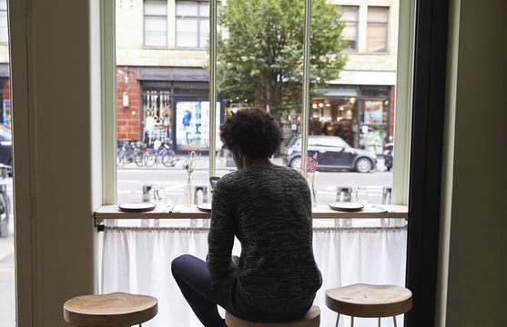 Rear View Of Young Man By Window Using Mobile Phone In Cafe