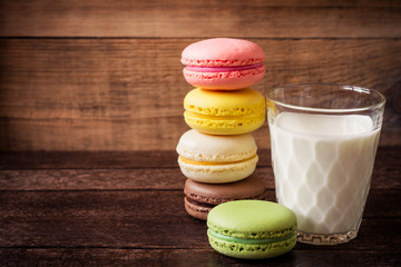 Colorful macarons and glass of milk on dark wooden background