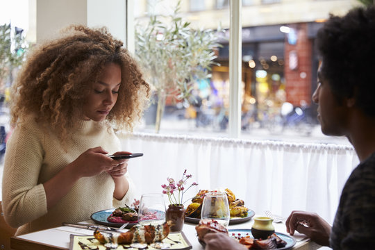 Young woman taking picture of meal in restaurant on mobile