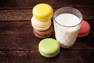 Colorful macarons and glass of milk on dark wooden background