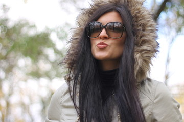 Beautiful woman with long dark hair giving kiss wearing hood in the autumn park 