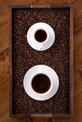 two cups of coffee on a tray full of beans