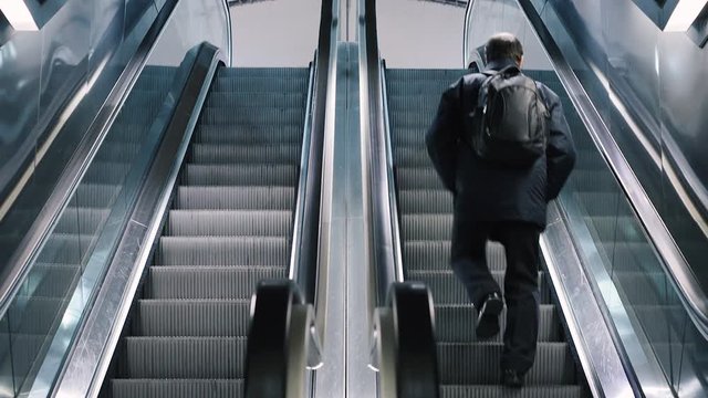 Man alone walks fast up stairs instead of riding the escalator. Modern escalator stairs moving up.