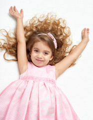 girl child with long hair lie on white and open arms, dressed in pink