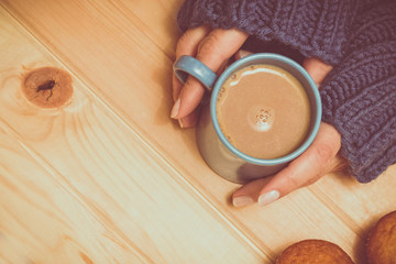 A cup of cocoa in the hands on a wooden background. Blue sweater