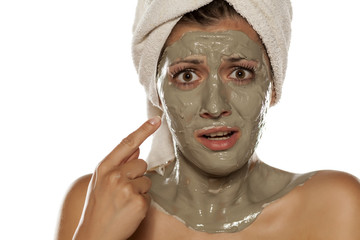 upset woman pointing a finger on the green clay mask on her face