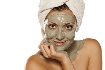 young woman with a towel on her head posing with a mask from green clay on her face