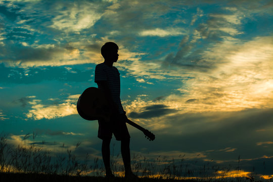 Man holding a guitar in the middle of a meadow silhouette