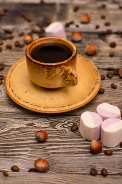Small cup of coffee with cocoa beans, hazelnuts and marshmallow on wooden background