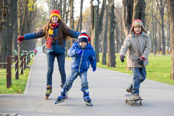 Three kids learning to ride in autumn park on rollerblades