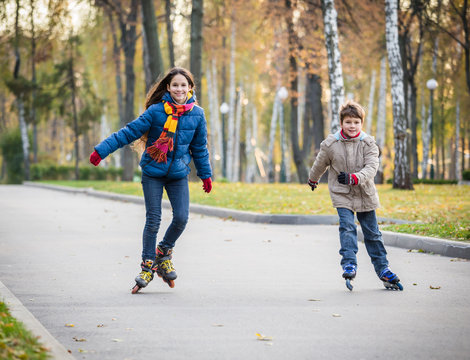 Two happy kids ride in autumn park on rollerblades
