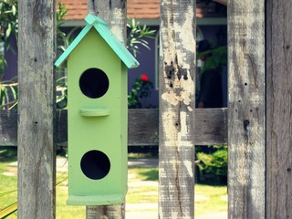 Old bird house or nest box hangs on the wooden fence.