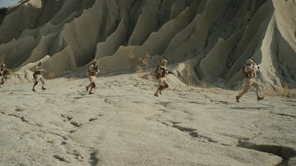  Squad of Fully Equipped and Armed Soldiers Running in a Single File in the Desert. Show Motion. Shot on RED EPIC Cinema Camera in 4K (UHD).