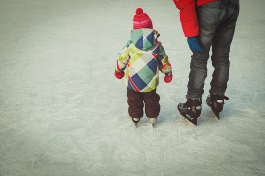 father teaching little daughter to skate in winter