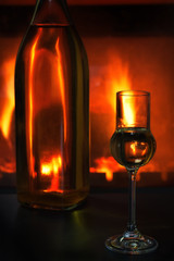 Flasche und Glas mit Likör vor brennendem Kaminfeuer auf schwarzem Tisch
