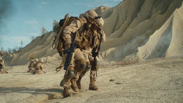  Soldiers Carrying Injured One While other Members of Squad Covering Them During Military Operation in the Desert. Slow Motion. Shot on RED EPIC Cinema Camera in 4K (UHD).
