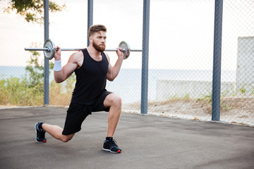 Concentrated young bearded sports man doing squatting exercises with barbell