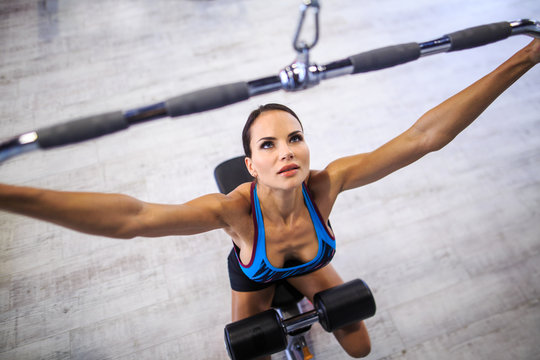 close-up, portrait of a girl in the gym. Girl doing exercise on the back muscles in a block simulator. Profel, girl's head rolled a little to us. Girl dressed in a pink top