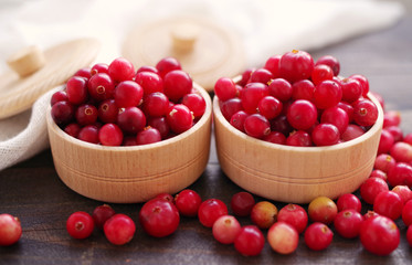 Fresh juicy cranberry in wooden round bowls on a table, close up