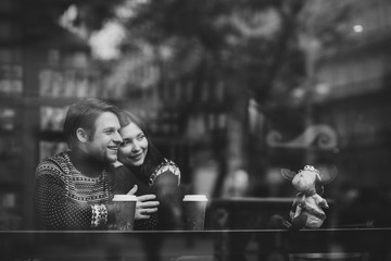 Happy and romantic caucasian couple in warm sweaters drink coffee from disposable paper cups in cafeteria. Holidays, christmas, winter, love, hot drinks, people concept