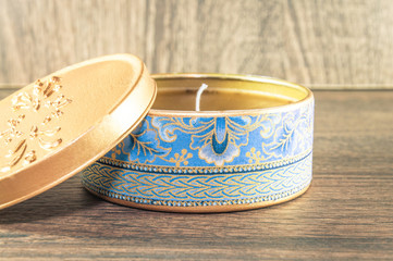 Handmade candle made in the golden rounded box decorated with textured fabric. Scenery and wooden background.