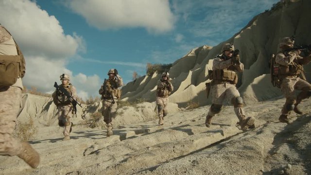 Squad of Fully Equipped and Armed Soldiers Running Forward During Military Operation in the Desert. Slow motion.