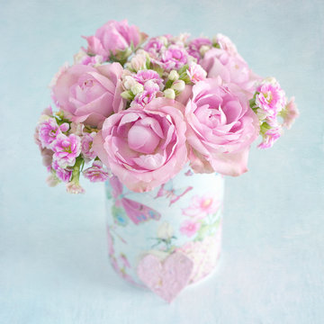Lovely bunch of a pink flowers in a vase ,decorated with a heart on a table .