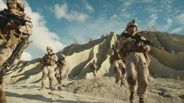 Squad of Fully Equipped and Armed Soldiers Walking in Single File in the Desert. Slow Motion.